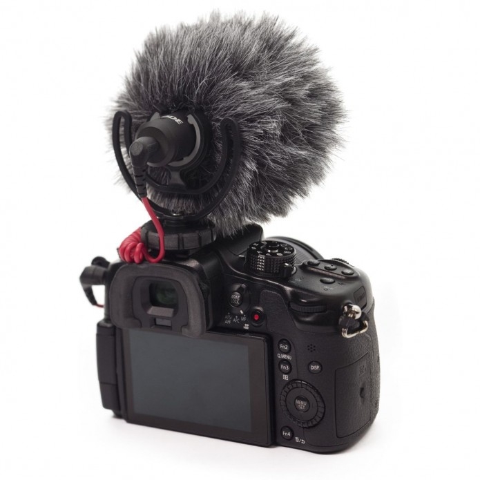 Das kompakte Røde VideoMicro On-Camera-Richtmikrofon mit montiertem, fellartigen WS9-Windschutz (Deadcat), aufgesteckt auf dem Blitzschuh einer schwarzen DSLR- oder Systemkamera in der Rückansicht auf weißem Hintergrund.