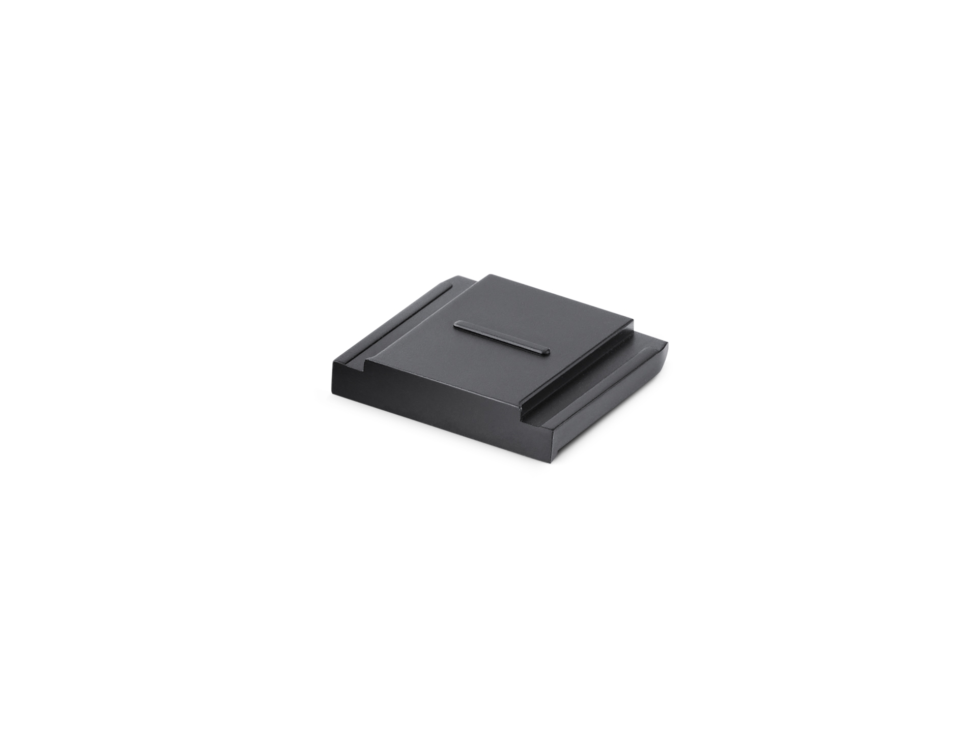 Ein kleines, rechteckiges Leica Hotshoe Cover aus schwarz eloxiertem Aluminium, schräg von oben zentriert vor einem rein weißen Hintergrund fotografiert. Die flache Blitzschuhabdeckung hat ein minimalistisches Design mit einer stufenförmigen Erhöhung auf