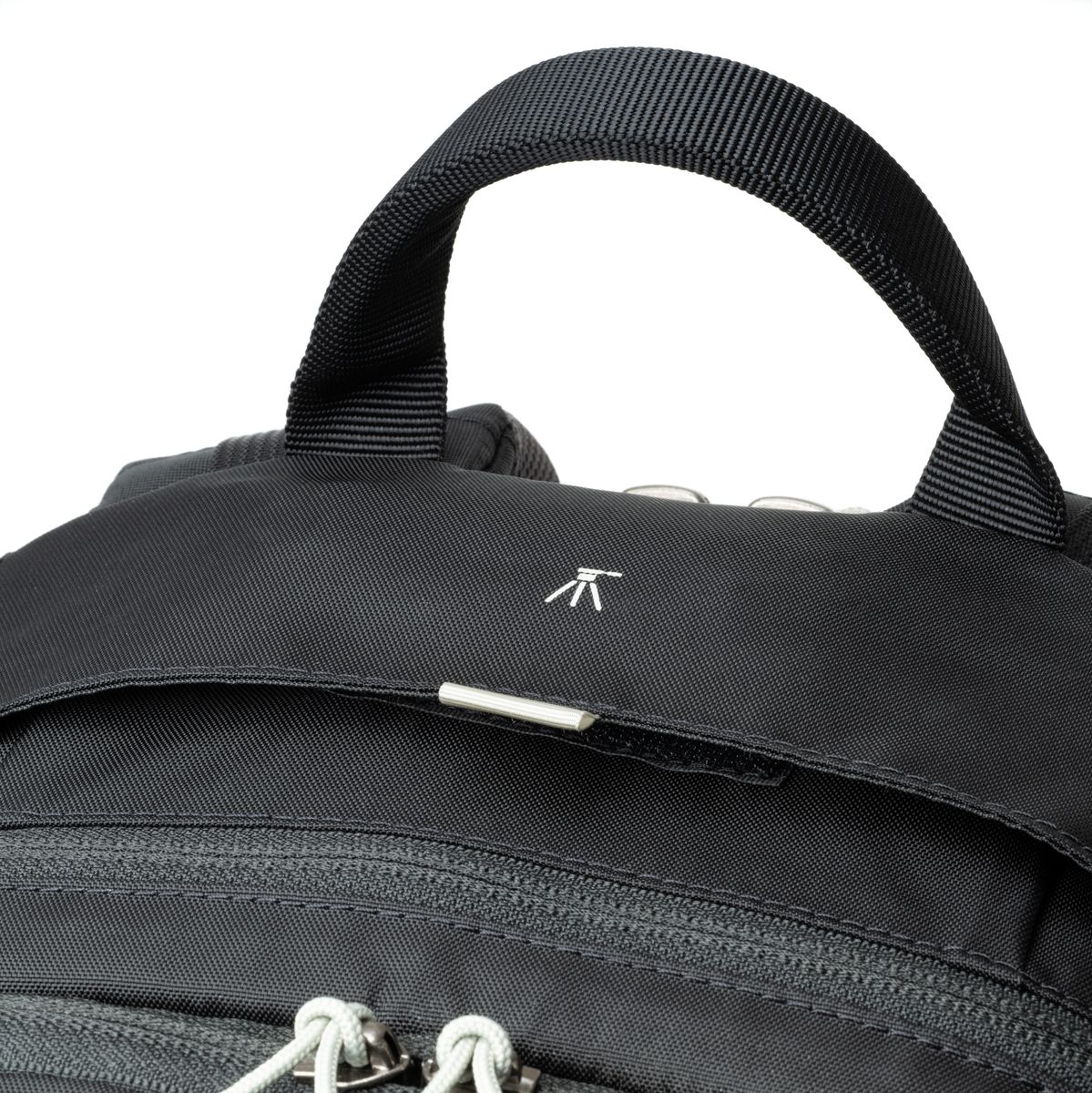 Detailansicht eines schwarzen Kamerarucksacks mit gepolstertem Tragegriff, Reißverschluss und kleiner Stativ-Markierung.