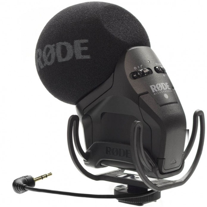 Das schwarze Røde VideoMic Pro+ On-Camera-Richtmikrofon in einer Dreiviertelansicht von hinten vor weißem Hintergrund, ausgestattet mit einem großen Schaumstoff-Windschutz samt grauem Røde-Logo, der integrierten Rycote Lyre Schockabsorber-Halterung, Bedie
