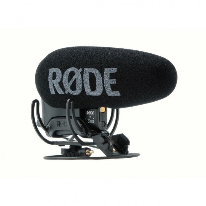 Das schwarze Røde VideoMic Pro+ On-Camera-Richtmikrofon in einer seitlichen Profilansicht von links vor weißem Hintergrund, ausgestattet mit einem großen Schaumstoff-Windschutz samt markantem grauen RØDE-Schriftzug, montiert in einer elastischen Rycote Ly