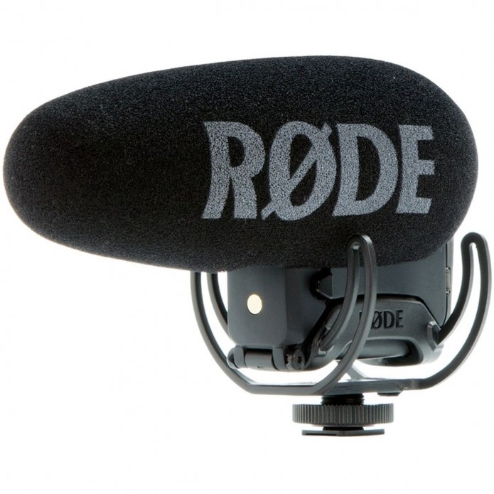 Das schwarze Røde VideoMic Pro (oder VideoMic Pro+) On-Camera-Richtmikrofon in einer seitlichen Profilansicht vor weißem Hintergrund, ausgestattet mit einem großen Schaumstoff-Windschutz samt markantem grauen RØDE-Schriftzug, montiert in einer elastischen