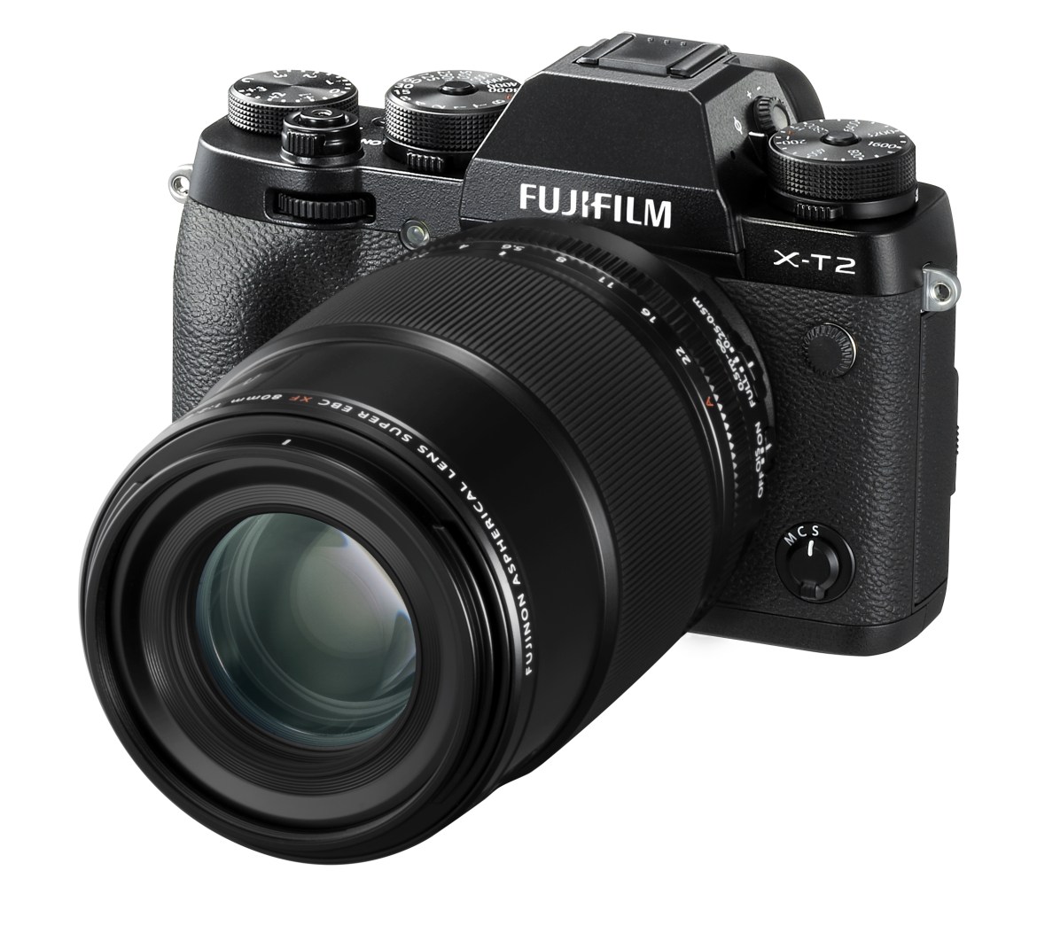 Schwarze Fujifilm X-T2 spiegellose Systemkamera in der schrägen Vorderansicht vor weißem Hintergrund, mit aufgesetztem großen, schwarzen Fujinon XF 80mm f/2.8 R LM OIS WR Macro Objektiv und sichtbaren analogen Einstellrädern auf der Gehäuseoberseite.
