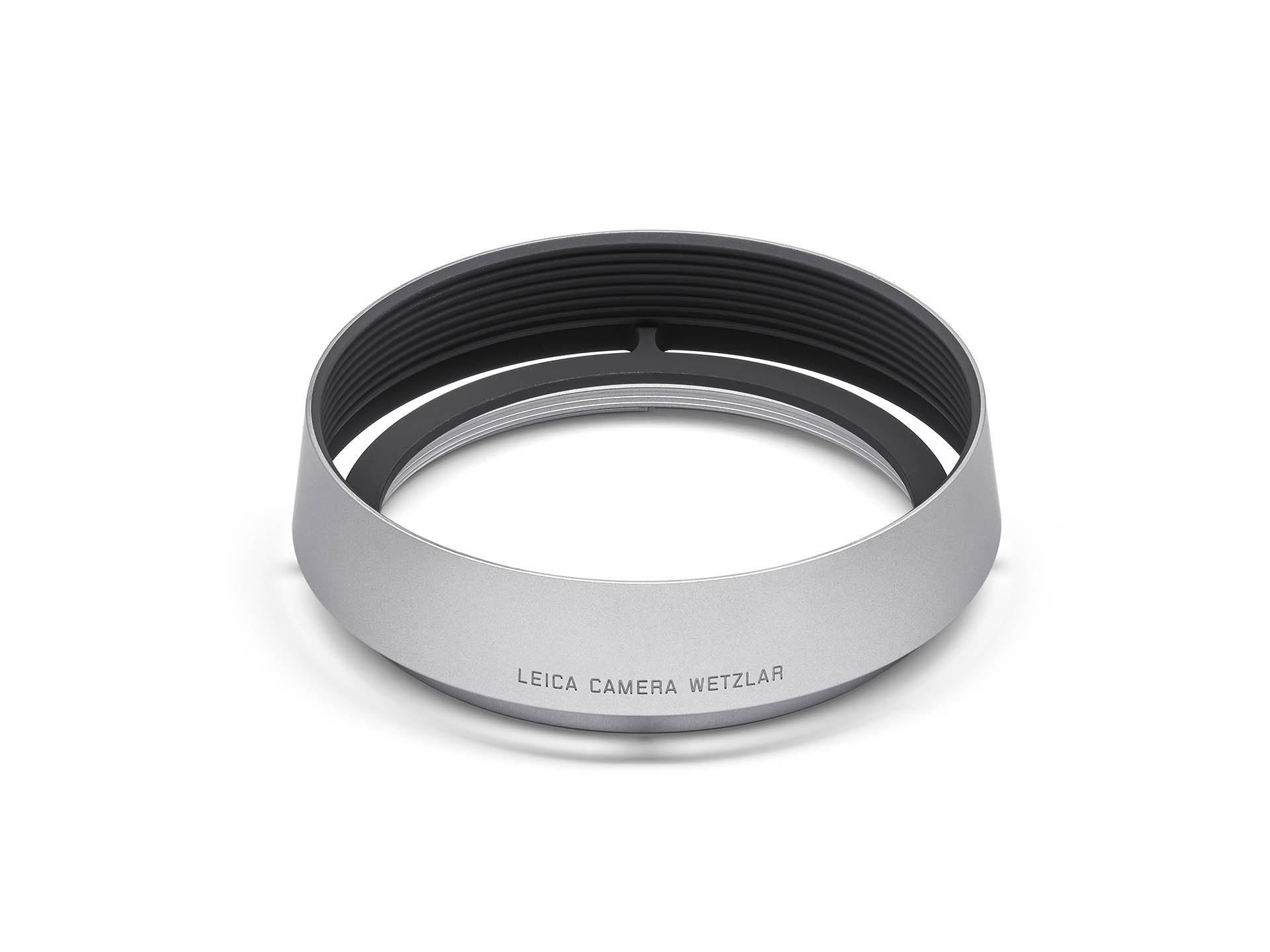 Eine runde, silbern eloxierte Leica Gegenlichtblende aus Aluminium, freigestellt auf einem weißen Hintergrund. Das Zubehörteil im Retro-Look ist für Kompaktkameras der Leica Q-Serie (wie Q, Q2 oder Q3) konzipiert. Auf der matten, silbernen Außenseite ist