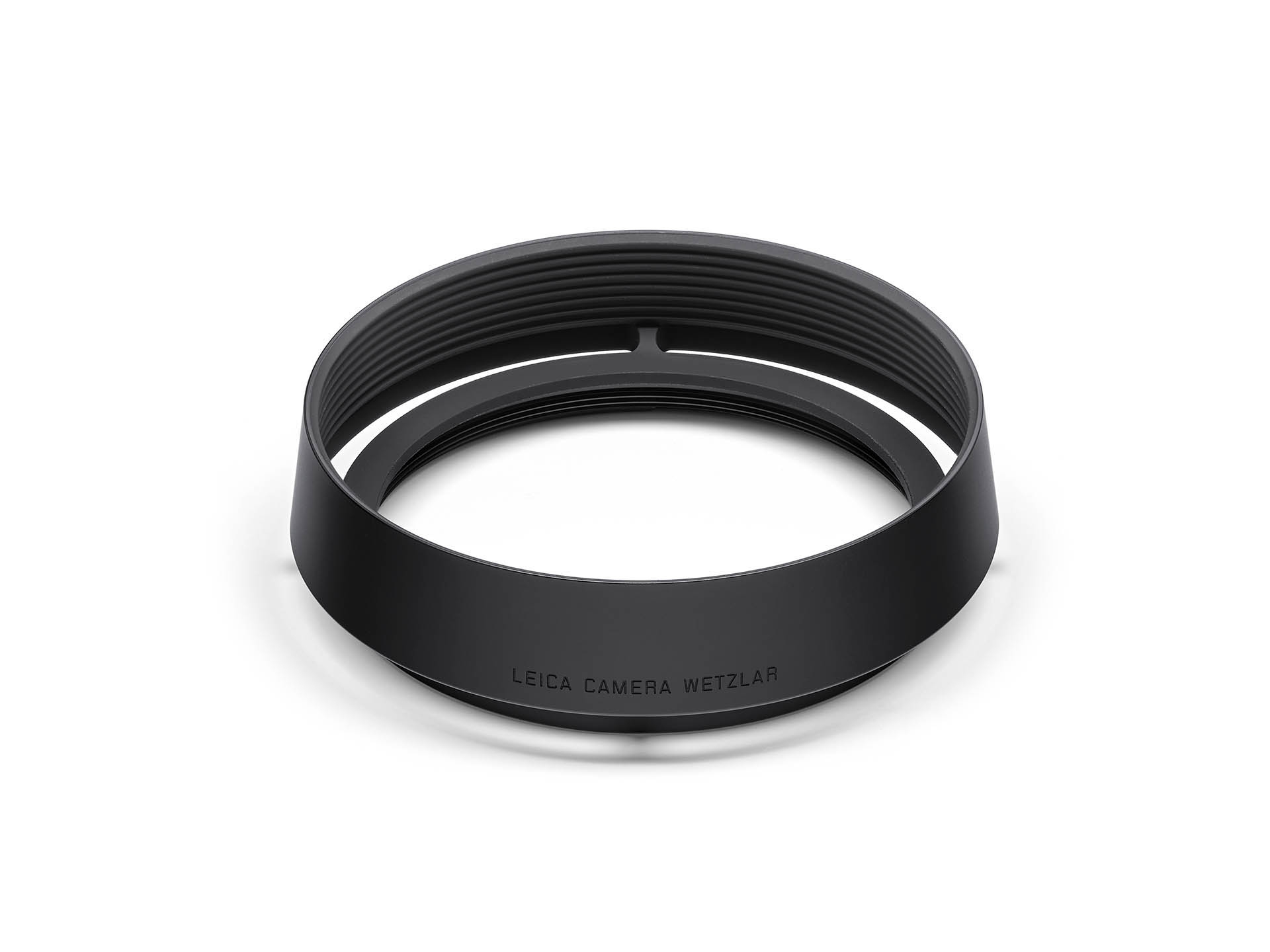 Eine kreisrunde, schwarz eloxierte Leica Gegenlichtblende aus Aluminium, leicht schräg von oben vor einem rein weißen Hintergrund fotografiert. Das Zubehörteil im minimalistischen Retrolook ist für Kompaktkameras der Leica Q-Serie (wie Q, Q2, Q3) gefertig