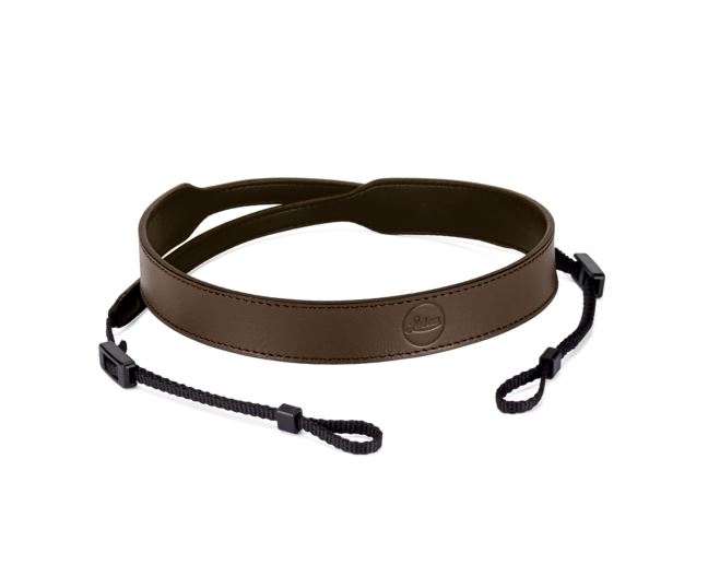 Perspektivische Draufsicht des elegant konturierten Leica C-Lux Kamera-Tragriemens aus feinem taupefarbenem Leder mit eingeprägtem runden Leica-Logo und schwarzen Befestigungsschlaufen vor weißem Hintergrund.
