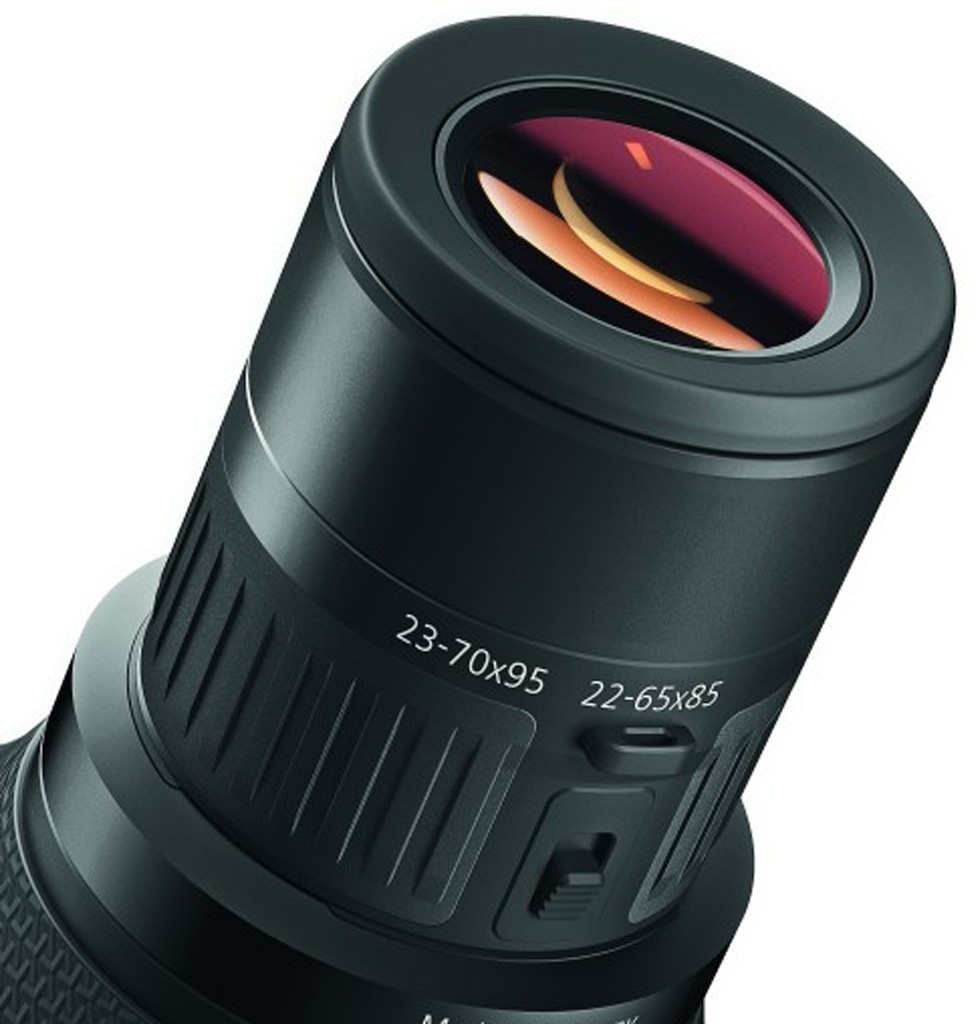 Eine Nahaufnahme des schwarzen ZEISS Victory Harpia 22-65x / 23-70x Okulars für Spektive vor weißem Hintergrund. Die obere Glaslinse zeigt eine ausgeprägte rötlich-violette und orangefarbene Antireflexbeschichtung. Am gummierten Gehäusering sind die weiße