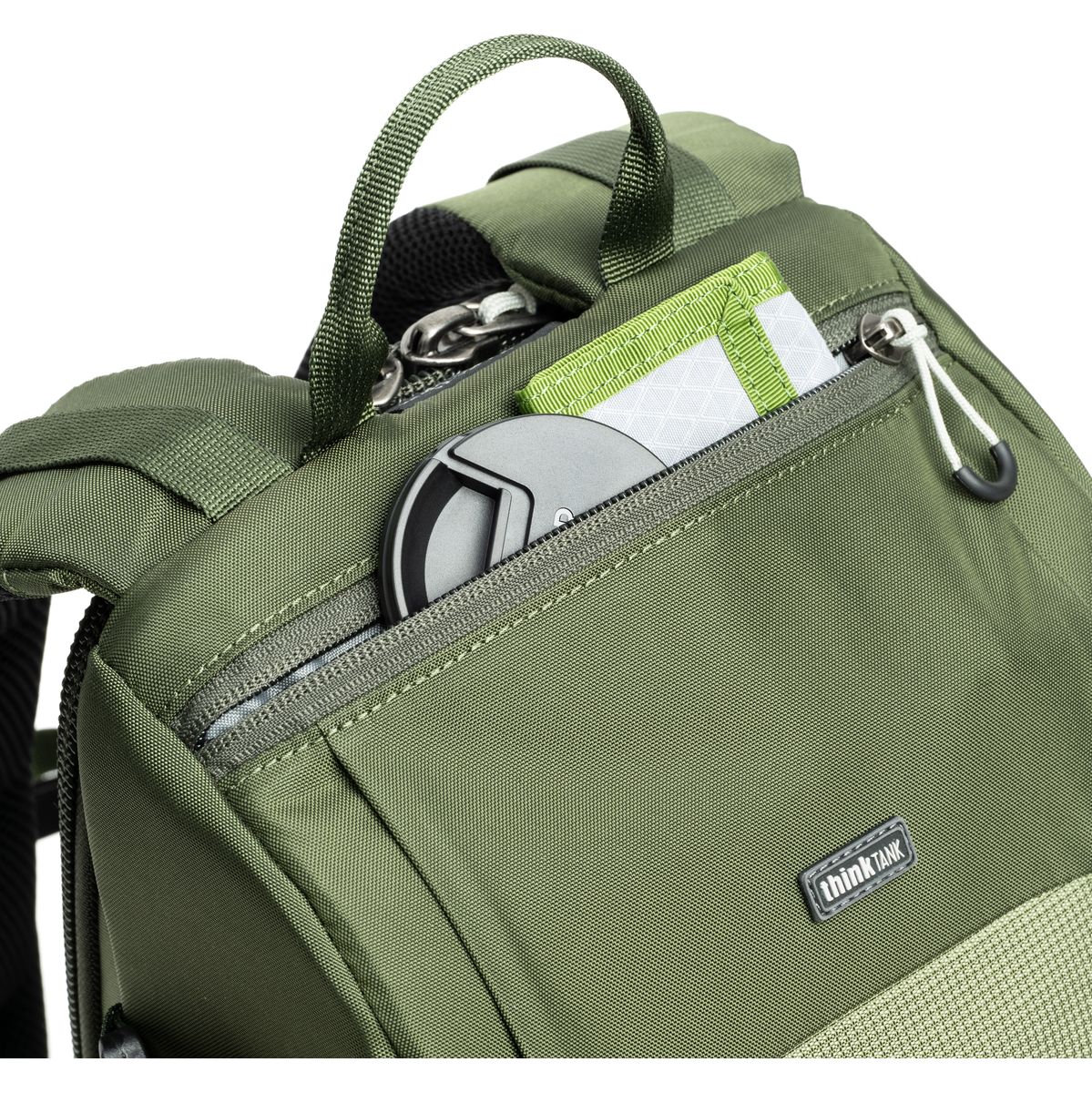 Detailansicht eines grünen Kamerarucksacks mit geöffnetem Reißverschlussfach, Tragegriff und eingesteckten Karten bzw. Zubehörteilen.