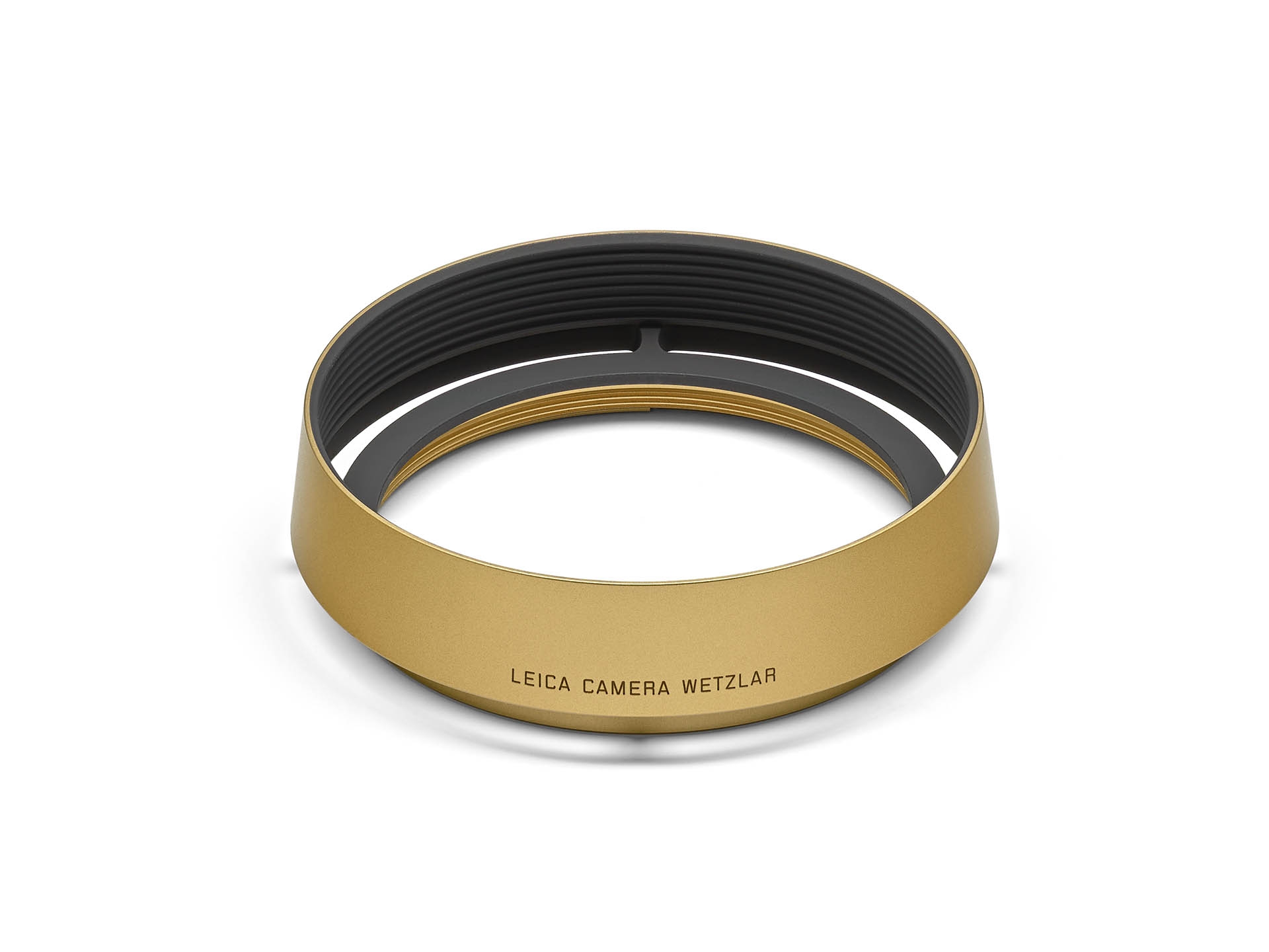 Eine kreisrunde, goldfarben eloxierte Leica Gegenlichtblende aus Aluminium, leicht schräg von oben vor einem rein weißen Hintergrund fotografiert. Das hochwertige Zubehörteil ist für Kompaktkameras der Leica Q-Serie (wie Q, Q2, Q3) gefertigt. Auf der matt