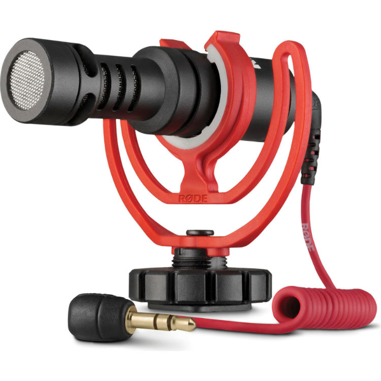 Schräge Frontansicht des kompakten Rode VideoMicro On-Camera-Mikrofons in der roten Rycote Lyre Schockabsorber-Halterung mit angeschlossenem roten 3,5-mm-Klinkenkabel (TRS) auf weißem Hintergrund.