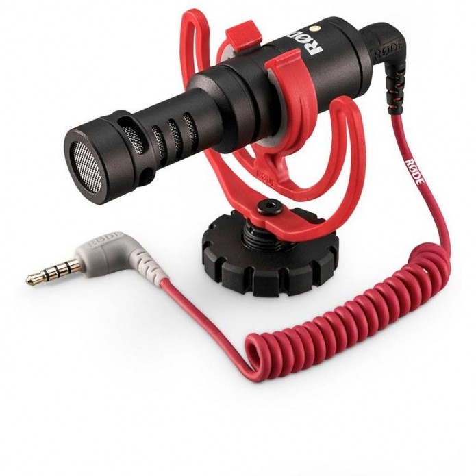 Das ultra-kompakte Røde VideoMicro On-Camera-Richtmikrofon in einer schrägen Dreiviertelansicht vor weißem Hintergrund, montiert in der markanten roten Rycote Lyre Schwinghalterung inklusive rotem 3,5-mm-TRS-Spiralkabel zur störungsfreien Tonübertragung a